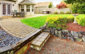 Garden with lawn, cobblestone path and stone wall.
