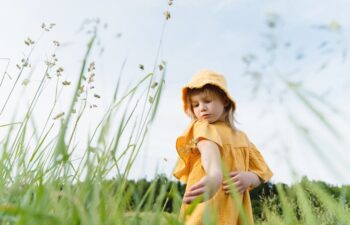 Little girl looking for insects on her skin while standing in tall grass in nature at summer. Child looking on the skin for tick or mosquito bite in meadow outdoors.